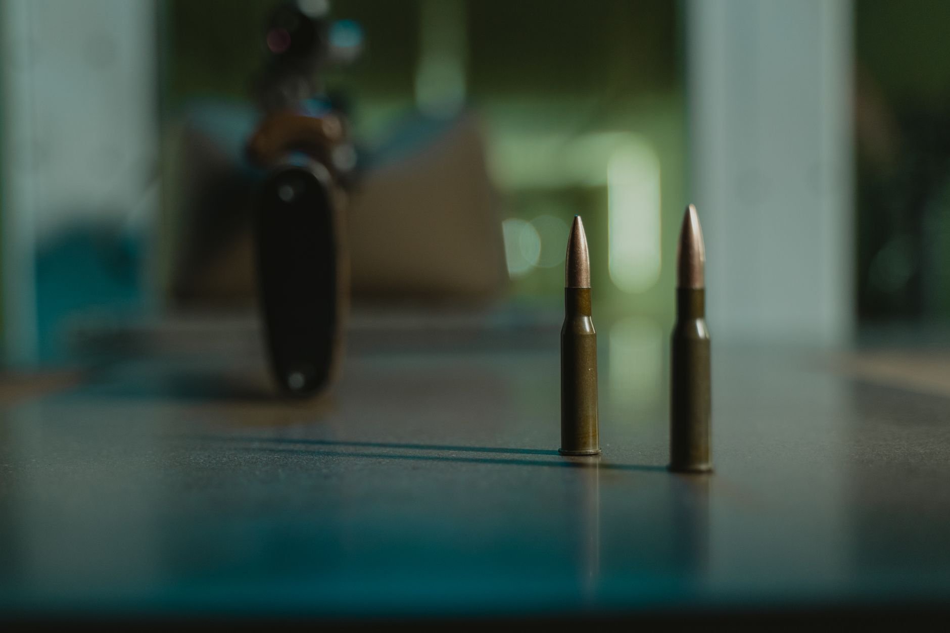 Two bullets on a table with a blurred rifle background in moody lighting.